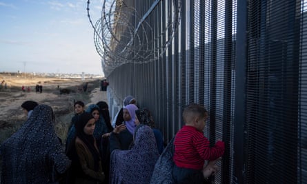 Palestinians displaced by the Israeli bombardment of the Gaza Strip peer through the border fence with Egypt in Rafah