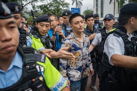 A former pro-democracy district councillor leaves the West Kowloon Magistrates' Courts flanked by police