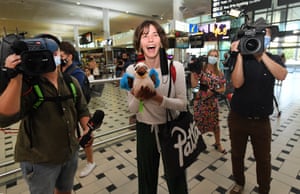 A woman holds a toy kookaburra and is smiling at the cameras as she arrives at the Brisbane international airport surrounded by photographers