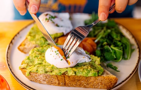 A breakfast plate with brown toast, poached eggs, avocado and spinach.