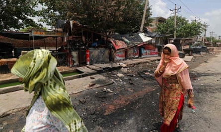 Women walk past burned shops after violence in Nuh.