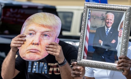 one person holding an image of trump next to another holding an image of biden