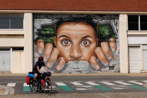 A cyclist passes a mural depicting someone peering through a hole in a wall