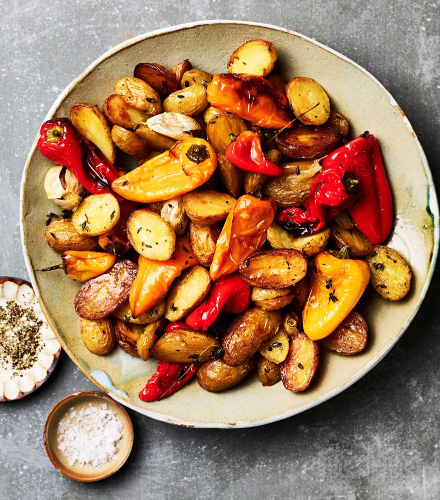 A round dish of roast potatoes with whole red and yellow peppers and garlic