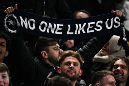 A Millwall fan holding a scarf emboldened with the club’s famous motto, “No one likes us”