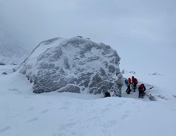 La roca donde se refugiaron los escaladores, rodeada de nieve con tres personas cerca