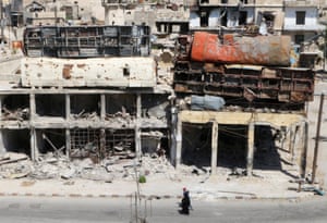 People walk past damaged buses positioned on top of buildings as barricades in the rebel-held Bab al-Hadid area