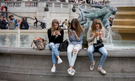 Teenage girls on their smartphones in the middle of Trafalgar Square, London
