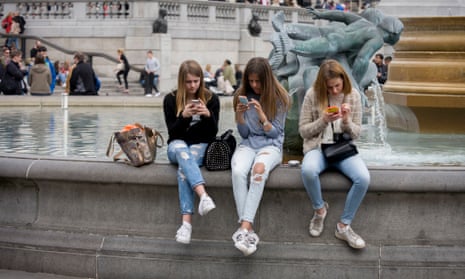 Teenage girls on their smartphones in Trafalgar Square, London.