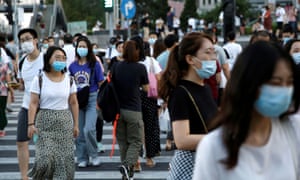 People wearing face masks walk across a street at a shopping area in Beijing, China 25 August 2020.