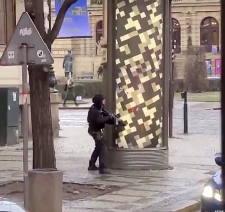 A figure in black with a gun behind a pillar.