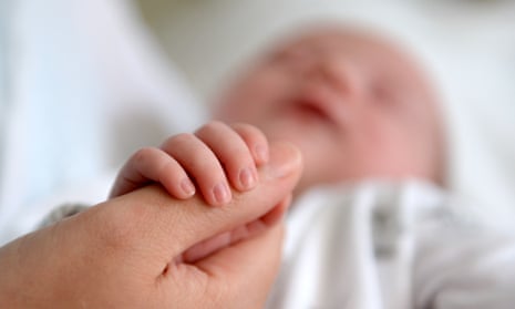 A newborn baby grasping the thumb of her mother
