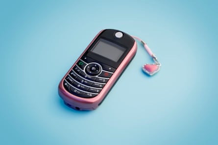 A 2000s era mobile phone with a pink charm hanging from the top, on a blue background.