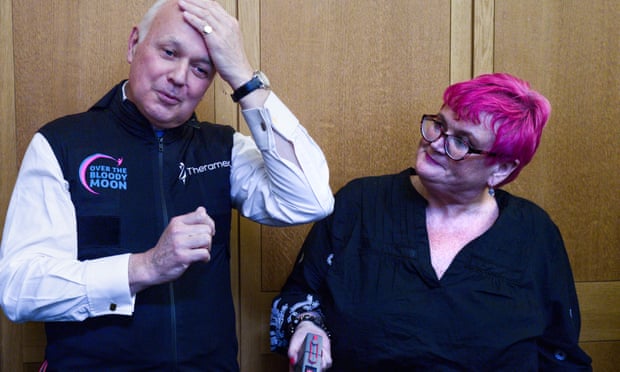 Iain Duncan Smith, wearing a MenoVest, pus one hand to his forehead, while Carolyn Harris looks on.