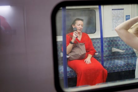 A woman sitting in an underground train carriage cooling herself with a portable fan
