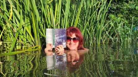 A woman submerged to the shoulders in water, holding a book with reeds behind her
