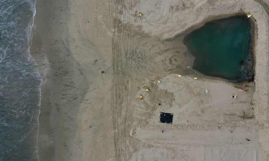 Crews clean up oil in a pool that flowed in from the high tide and was held back by a sand berm and boom, on the border of Huntington Beach and Newport Beach on Monday.