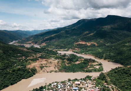 Guanay, the seat of the Guanay municipality, seen from the air, with a muddy river running through a wooded landscape.