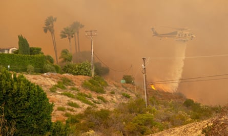 A Los Angeles County Fire Department Sikorsky S-70 Firehawk helicopter works to save a home from the encroaching flames of the Woolsey Fire.
