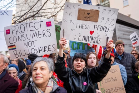 People hold signs that read ‘protect consumers not billionaires’ and ‘these people heart consumers’