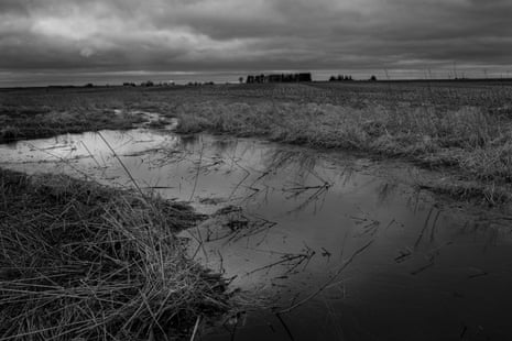 A vast field with a large puddle in the middle of it.