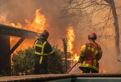 Two firefighters stood near a wildfire.