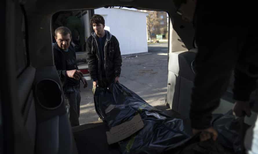 Volunteer, Payton Robinson, center, from the United States, prepares to carry the body of a Russian soldier to a refrigerated container in Bucha, Ukraine.