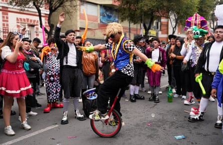 A clown rides a unicycle during a protest in La Paz with people in costumes surrounding him