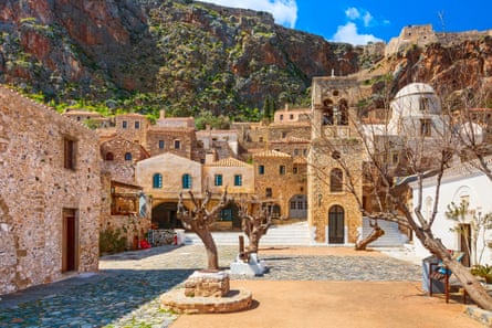 A town square with a stunted trees and a cliff in the background