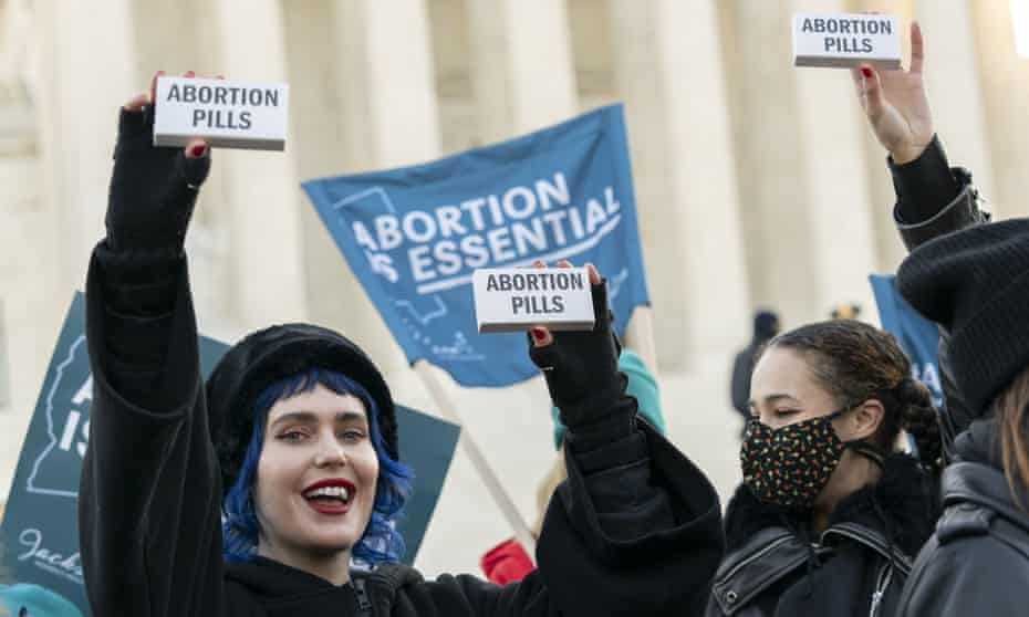 Women protest showing signs saying abortion pills and abortion is essential