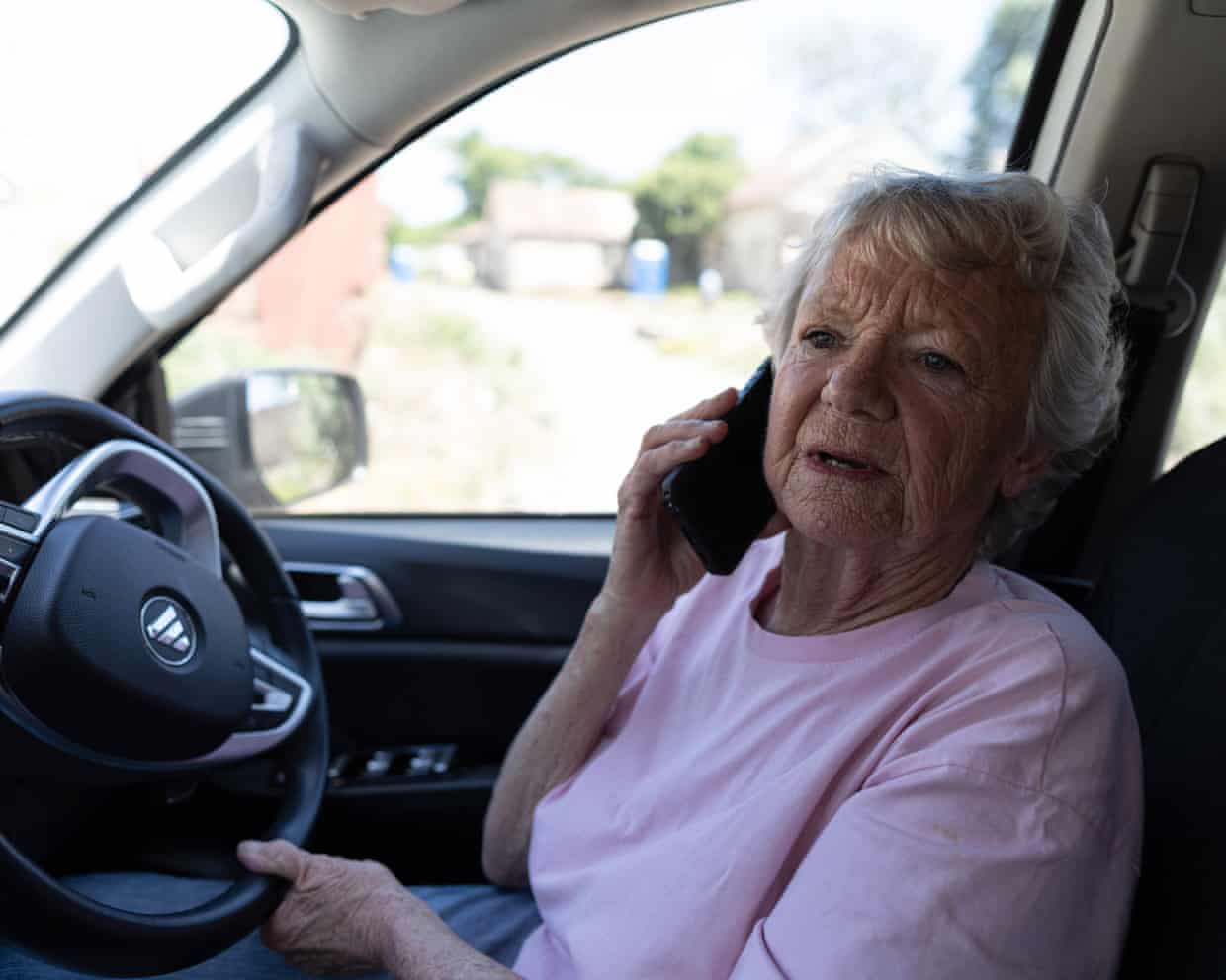 Cora Bailey, an elderly woman with grey hair, talks on a mobile phone while sitting in a car