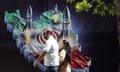 A man and a woman walk past a billboard with an illustration showing missiles taking off from a stylised 3D relief map of Iran