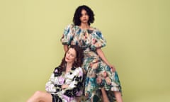 Two female models sit together, with dour expressions. One has long brown hair and wears a black, white and lilac print dress. The other has brown coils and wears a voluminous dress with a multicoloured print.