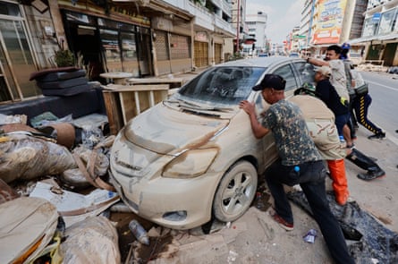 People try to move a mud-covered car on a street