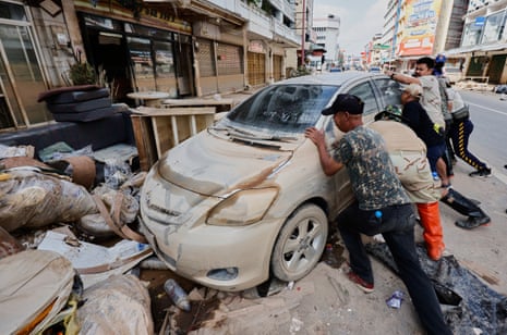 People try to move a mud-covered car on a street