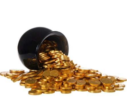 A black pot lies tipped over, spilling a large pile of gold coins on to a white surface