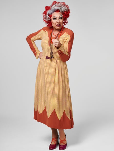 A drag queen in a red and grey wig looking cross and pointing a finger at the camera.