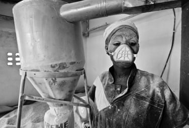 A female miller wearing a mask covering her nose and mouth, covered in dust after processing grains into cornmeal