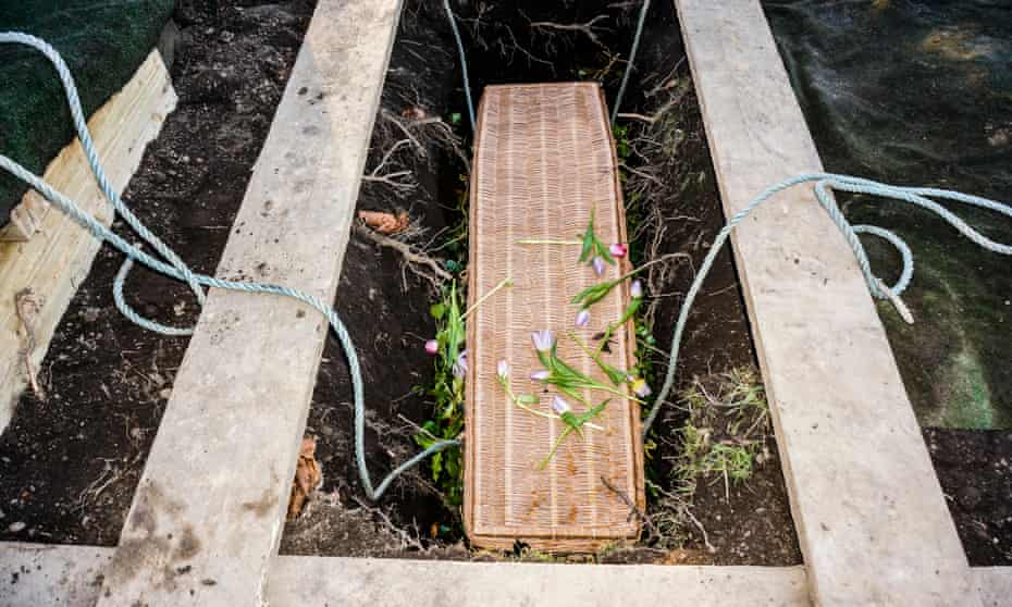 A wicker coffin is lowered into a grave