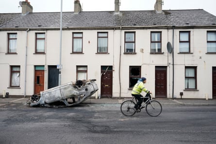 A man cycles past a burnt-out overturned car in Ballymena
