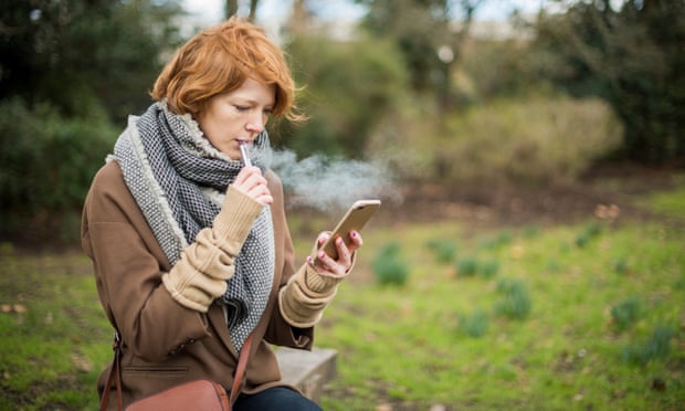 A young woman vapes while she checks her phone.
