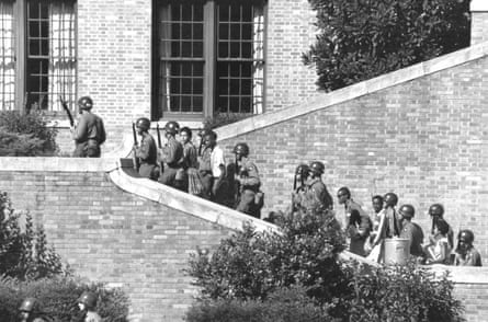 Armed men in uniform escort children up a staircase