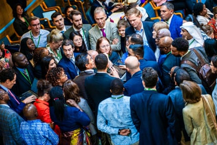 A cluster of about 50 people from all around the world standing close together in a hall as they discuss something
