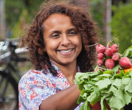 A woman smiles at a bunch of radishes.