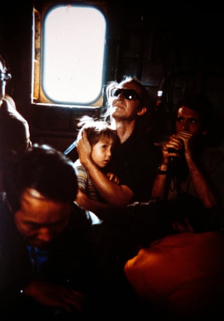 A western civilian clutches a child in a crowded military helicopter.