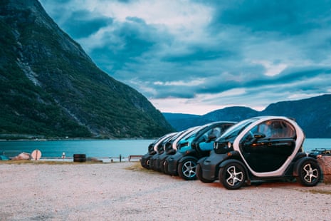 Electric cars parked in a row next to a lake surrounded by steep mountains in Eidfjord, Norway