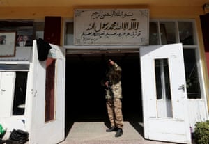 A Taliban fighter gestures to a colleague as he stands by the entrance to a school, in Kabul, Afghanistan.