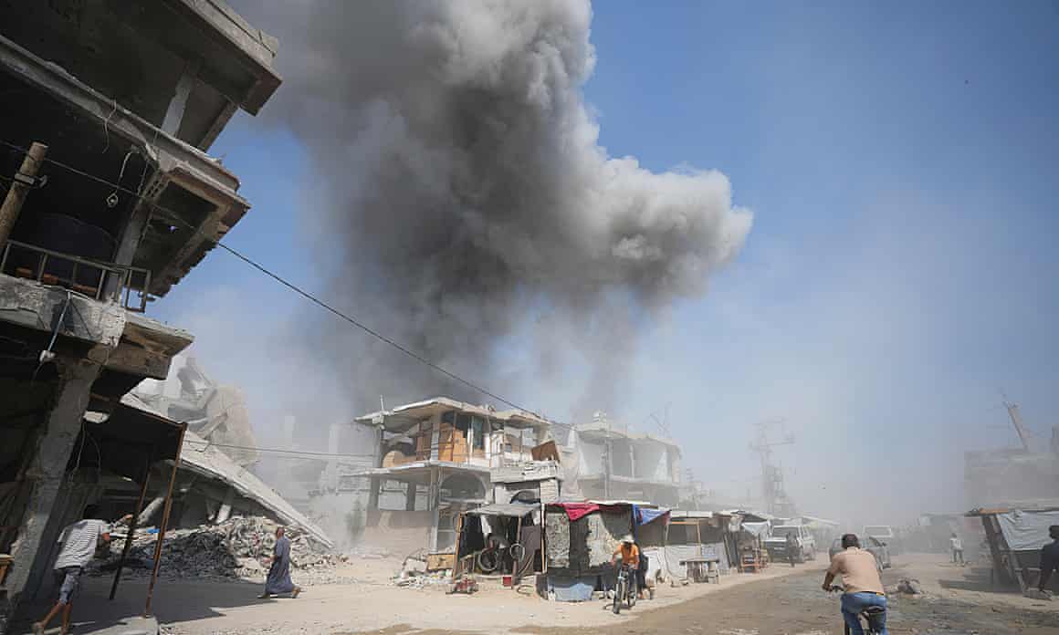 Smoke rises over a building on a street in Khan Younis, with other wrecked buildings in the foreground