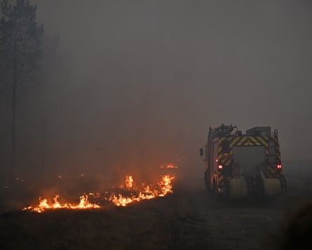 A fire engine drives through smoke past an area of burning scrub