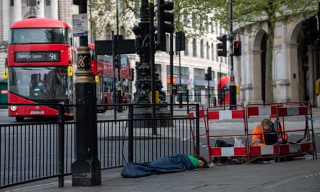 An electrician works on public services at Trafalgar Square, central London, while a homeless man sleeps next to him and buses go by